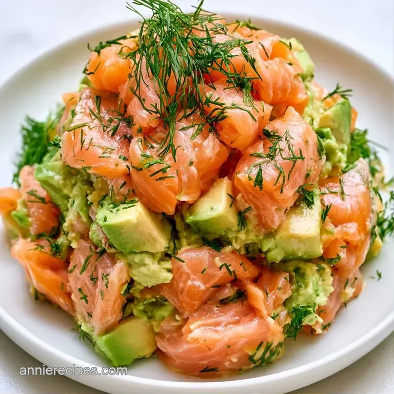 Two elegant towers of diced salmon and avocado on a white plate, accented by microgreens and a lemon wedge.