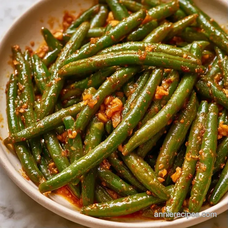 A white ceramic bowl filled with glistening green beans in a rich brown sauce, topped with fresh sliced scallions.