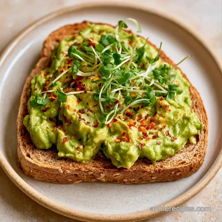 Sliced artisan toast topped with creamy avocado, red pepper flakes, and microgreens on a matte grey stone platter.